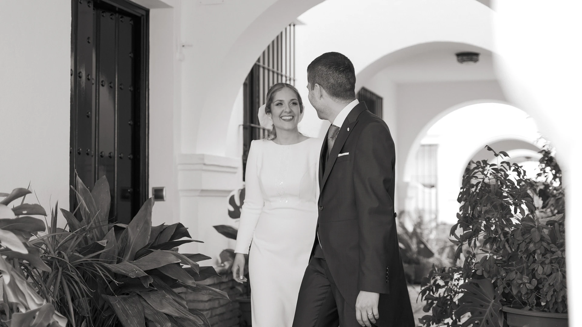 Álvaro y Patricia caminan bajo un arco blanco, en blanco y negro