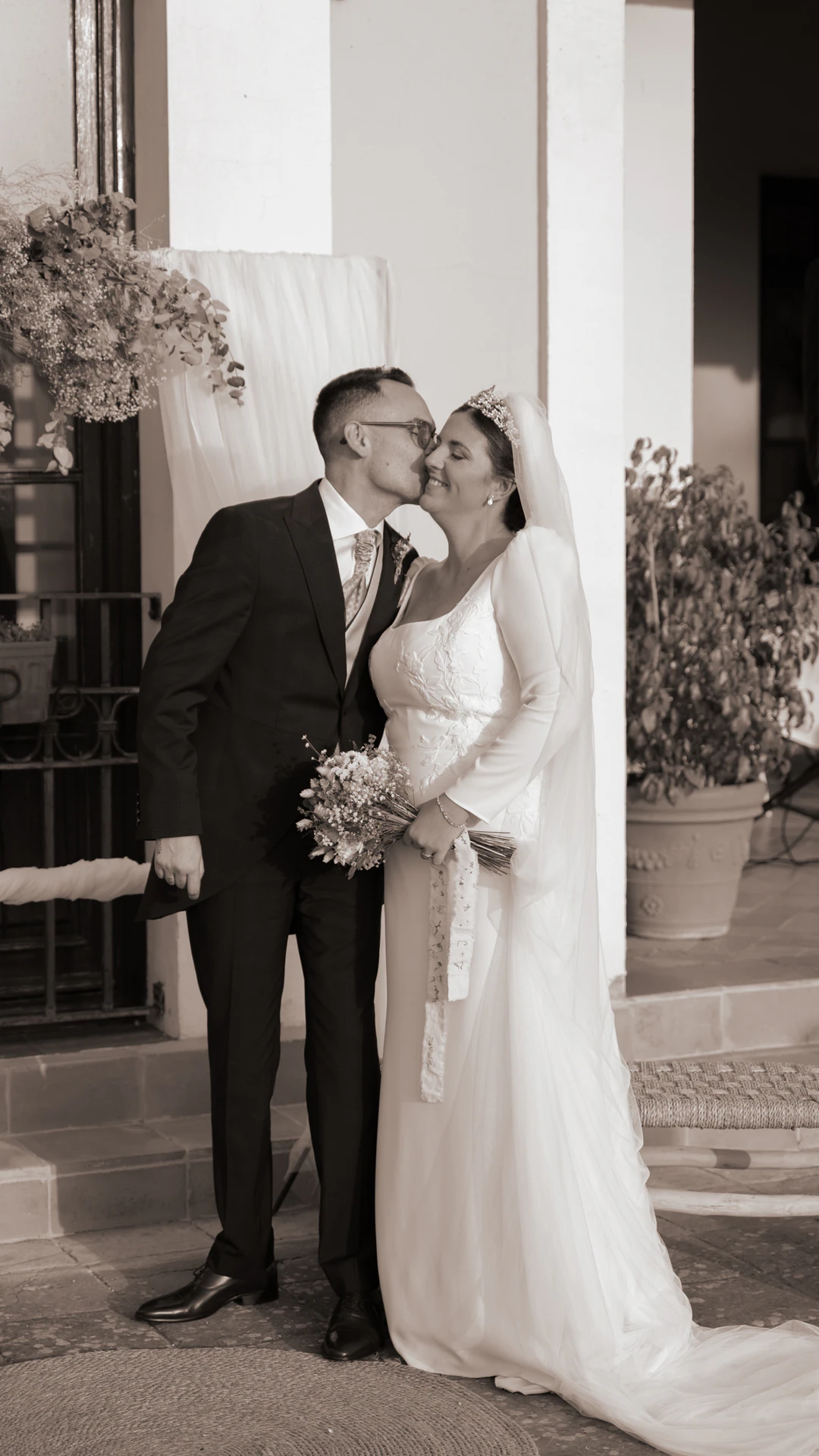 Jesús y Laura se besan junto a la puerta, en blanco y negro