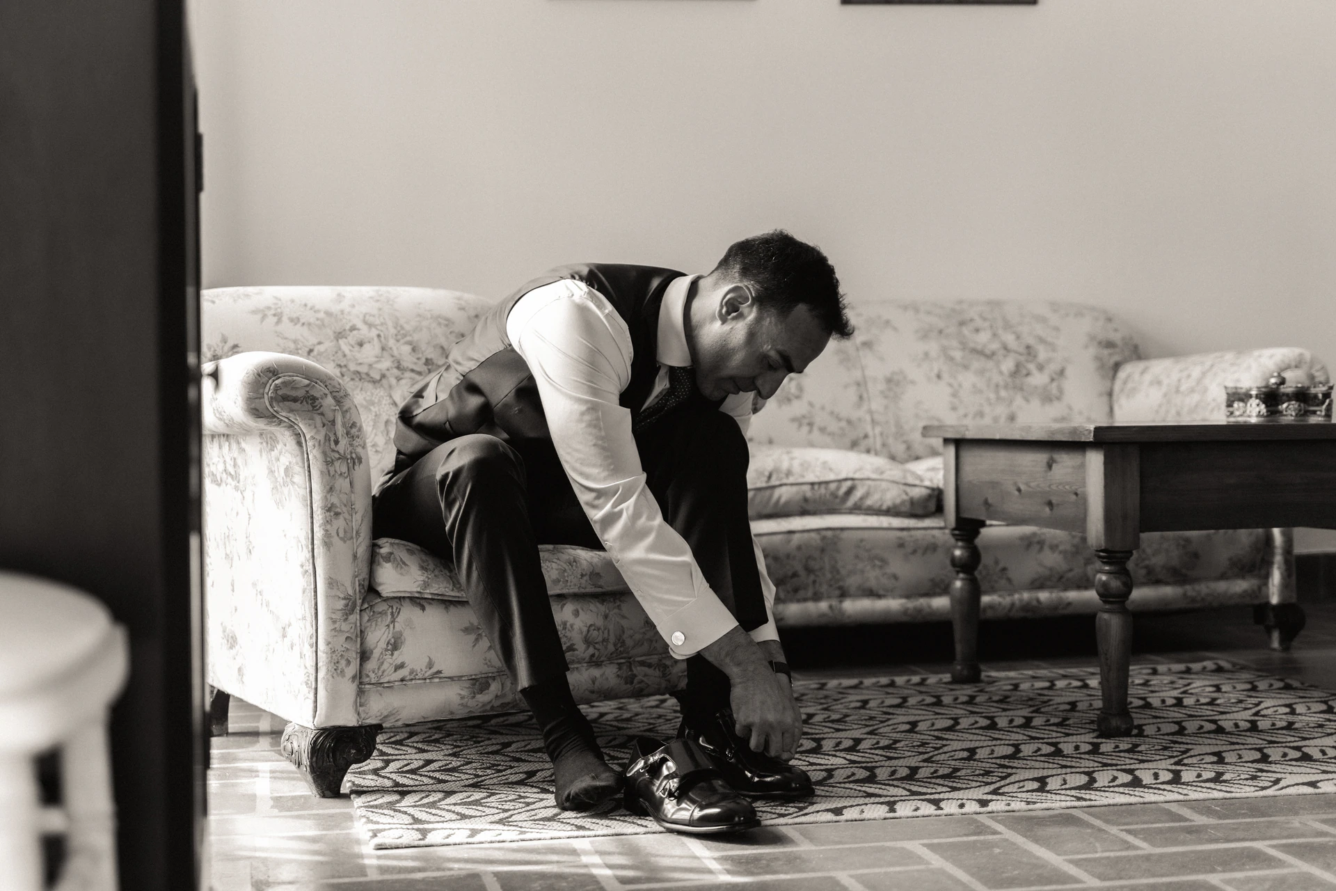 Fernando se calza sentado en un sofá, en blanco y negro