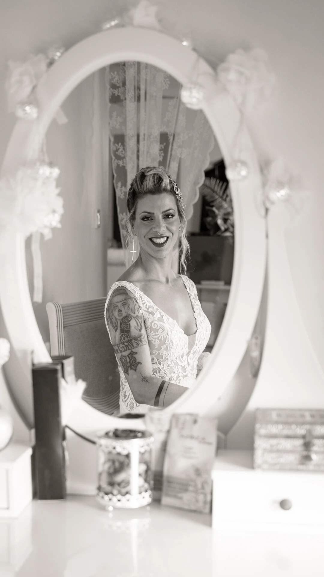 Una de las novias sonríe reflejada en el espejo de un tocador, en blanco y negro