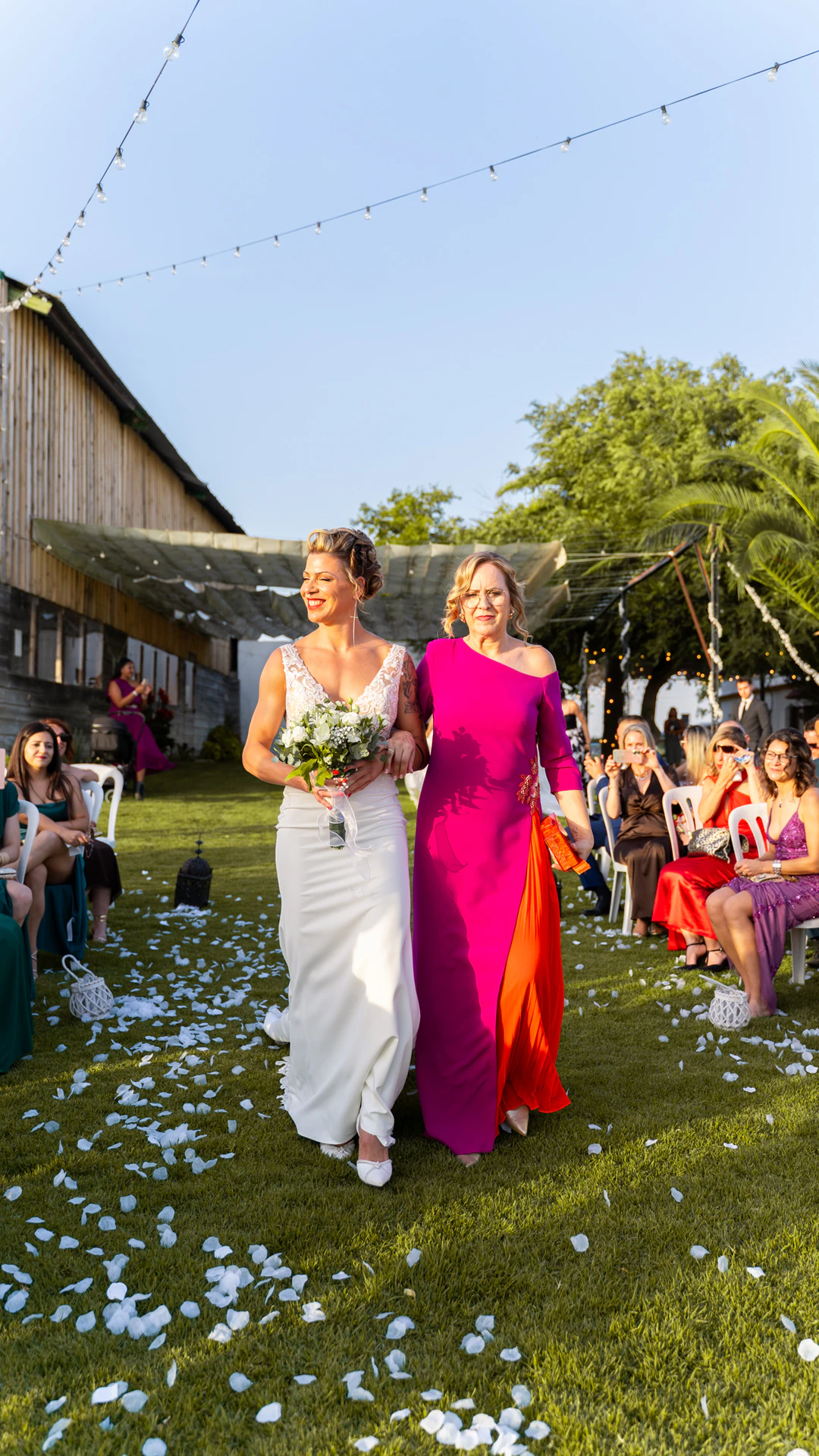 Una de las novias llega a la ceremonia del brazo de una mujer vestida de fucsia